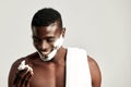 Studio portrait of handsome black guy with naked torso applying cream on his face. Afro American man with towel on his Royalty Free Stock Photo