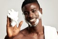 Studio portrait of handsome black guy with naked torso applying cream on his face. Afro American man with towel on his Royalty Free Stock Photo