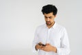 Studio portrait of handsome focused young man in shirt holding smartphone looking on device screen standing on white Royalty Free Stock Photo