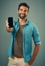 Take a look and tell me what you think. Studio portrait of a handsome young man holding a cellphone with a blank screen Royalty Free Stock Photo