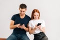 Studio portrait of happy addicted couple using browsing mobile phone looking at screen sitting on white isolated Royalty Free Stock Photo