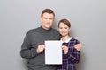 Portrait of adult couple holding together white blank paper sheet