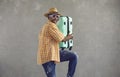 Studio portrait of happy black tourist in sun hat and sunglasses carrying travel suitcase Royalty Free Stock Photo