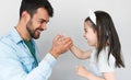 Studio portrait of happy handsome young father is thumb wrestling with his cute little daughter, isolated on grey wall. Smiling