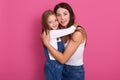 Studio portrait of happy mother and her little daughter hugging each other while posing in studio over rose background, wearing Royalty Free Stock Photo