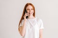 Studio portrait of happy redhead young woman having pleasant mobile conversation using smartphone and looking at camera Royalty Free Stock Photo