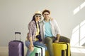 Studio portrait of happy young couple sitting on suitcases packed for holiday trip