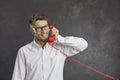 Studio portrait of a happy young man talking on red landline telephone on gray background. Royalty Free Stock Photo