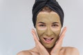 Studio portrait of happy young woman applying facial cosmetic green clay organic mask on her face, wears black towel on hair. Royalty Free Stock Photo