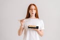 Studio portrait of happy young woman with closed eyes eating delicious sushi rolls with chopsticks standing on white Royalty Free Stock Photo