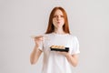 Studio portrait of hungry young woman eating delicious sushi rolls with chopsticks looking at camera standing on white Royalty Free Stock Photo