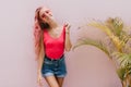 Studio portrait of joyful woman in denim shorts posing beside palm tree. Laughing gorgeous female m