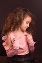 Studio portrait of little girl with long curly hair, in a pink skirt and black shorts, sitting on an office chair Royalty Free Stock Photo