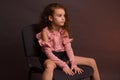 Studio portrait of little girl with long curly hair, in a pink skirt and black shorts, sitting on an office chair Royalty Free Stock Photo