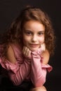 Studio portrait of little girl with long curly hair, in a pink skirt and black shorts, sitting on an office chair Royalty Free Stock Photo