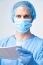 Studio Portrait Of Male Surgeon Wearing Gown And Mask Holding Medical Print Out