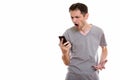 Studio shot of angry young man shouting while using mobile phone Royalty Free Stock Photo