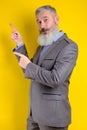 Studio portrait mature businessman dressed in gray suit points aside, I choose you this, yellow background Royalty Free Stock Photo