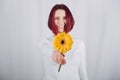 Studio portrait millennial woman with bright red Color hair and yellow flower.