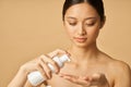 Studio portrait of natural young woman holding a bottle of gentle foam facial cleanser isolated over beige background Royalty Free Stock Photo