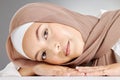 Studio portrait of one beautiful young muslim woman wearing brown headscarf lying against grey background. Happy arab Royalty Free Stock Photo