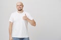 Studio portrait of positive bald european man holding thumbs up and smiling happily at camera while standing over gray Royalty Free Stock Photo