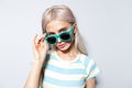 Studio portrait of pretty blonde girl in striped shirt taking off sunglasses. Royalty Free Stock Photo