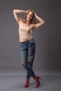 Studio portrait of pretty woman model with amazing body long legs leaning agains wall wearing denim jeans, lingerie top high heels Royalty Free Stock Photo