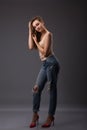 Studio portrait of pretty woman model with amazing body long legs leaning agains wall wearing denim jeans, lingerie top high heels Royalty Free Stock Photo