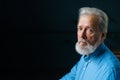 Studio portrait of sad gray-haired senior man unemotionally looking at camera on black isolated background. Royalty Free Stock Photo