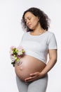 Studio portrait serene pretty pregnant woman with her eyes closed, holding bouquet of flowers in hand near her big belly