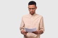 Studio portrait of serious African American young businessman in casual shirt analyzing financial reports posing on white studio