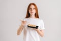 Studio portrait of serious young woman eating delicious sushi rolls with chopsticks looking at camera standing on white Royalty Free Stock Photo