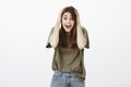 Studio portrait of shocked surprised cute girl in trendy t-shirt, holding hands on head and yelling from happiness