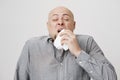 Studio portrait of sick bald caucasian man holding napkin or tissue, trying to cover mouth while sneezing with closed