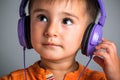 Studio portrait of a small funny boy with brown eyes in headphones listening to music on a gray background, emotions of joy, surpr Royalty Free Stock Photo