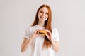 Studio portrait of smiling attractive redhead young woman holding tasty burger and looking at camera standing on white Royalty Free Stock Photo