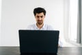 Studio portrait of smiling bearded man in shirt working typing on laptop computer looking to screen sitting at desk in Royalty Free Stock Photo