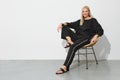 Studio portrait of smiling blonde woman in black casual clothes sitting on wicker chair Royalty Free Stock Photo