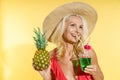 Studio portrait of smiling blonde woman in red swimsuit and straw hat looking away, drinking cocktail, holding fresh Royalty Free Stock Photo