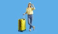 Portrait of happy female tourist standing with yellow suitcase on blue studio background Royalty Free Stock Photo