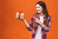 Studio portrait of smiling young beautiful woman holds red gift box. Isolated against orange background Royalty Free Stock Photo
