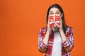 Studio portrait of smiling young beautiful woman holds red gift box. Isolated against orange background Royalty Free Stock Photo