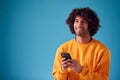 Studio Portrait Of Smiling Young Man Looking At Mobile Phone Against Blue Background Royalty Free Stock Photo