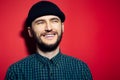 Studio portrait of smiling young man, wearing green plaid shirt and black beanie hat on red background. Royalty Free Stock Photo