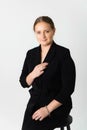 Studio portrait of a smiling young woman wearing black suit sitting on a chair against a gray background Royalty Free Stock Photo