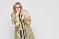 Surprised woman in glasses in golden coat covering mouth, pointing finger at blank copy space