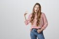 Studio portrait of surprised careless caucasian girl with blonde hair in striped sweater shaping something small over Royalty Free Stock Photo