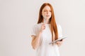 Studio portrait of thoughtful redhead young woman with closed eyes touch face with pen, holding diary standing on white Royalty Free Stock Photo