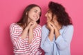 Studio portrait of two girls posing isolated over rose background, cute friends looking at each other with charming smiles and Royalty Free Stock Photo